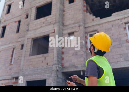 civil engineer or architect with hardhat on construction site checking schedule on smartphone Stock Photo