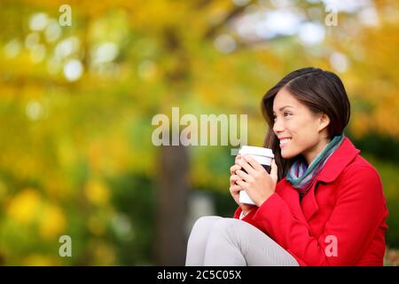 Autumn / fall woman drinking coffee looking at forest foliage copy space thinking. Happy smiling multi-ethnic Asian Chinese / Caucasian female model in red coat enjoying hot drink outdoor. Stock Photo