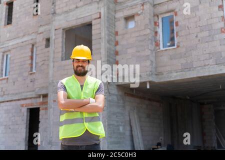 Construction worker looking at camera with hardhat in construction site background Stock Photo