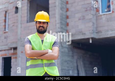 Construction worker looking at camera with hardhat in construction site background Stock Photo