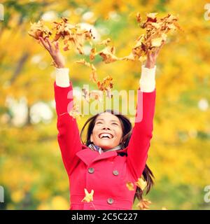 Autumn / fall woman happy throwing leaves up in the air with arms raised up towards the sky with smiling cheerful, elated expression of happiness. Beautiful girl in colorful forest foliage outdoor. Stock Photo