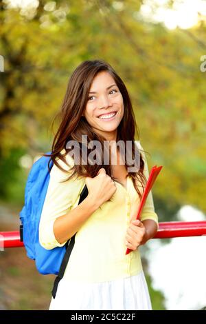 Young woman adult student in autumn park going back to school on university college. Asian girl smiling happy. Pretty mixed race Caucasian / Chinese Asian female model. Stock Photo