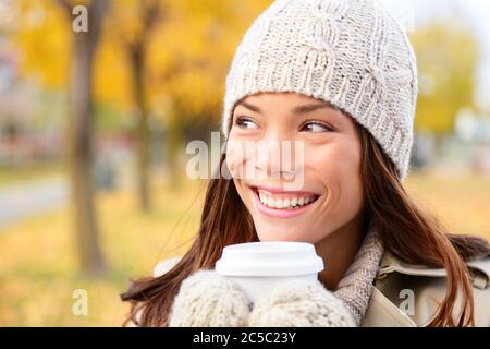 Autumn / fall woman drinking coffee looking at forest foliage copy space thinking. Happy smiling multi-ethnic Asian Chinese / Caucasian female model in red coat enjoying hot drink outdoor. Stock Photo