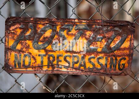 Rusty old dented posted no trespassing sign wired on a chain link fence Stock Photo