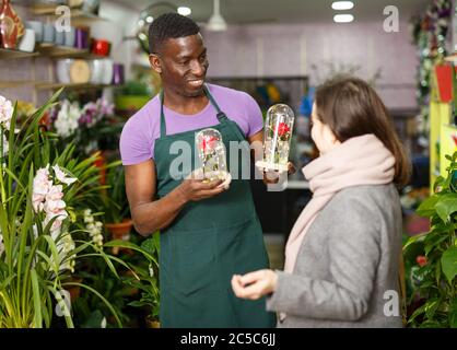 Smiling African American male florist helping female customer to choose flowers in gift box at flower shop Stock Photo