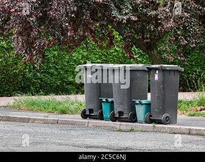Black bins with unrecyclable rubbish, alongside green bins with waste food, parked on the pavement awaiting collection during the weekly bin day. Stock Photo