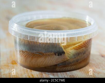 Pickled herring fillet in marinade of oil in plastic container Stock Photo