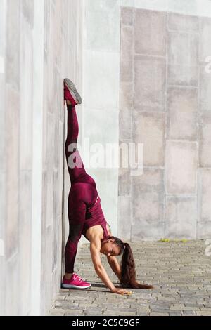 Girl athlete performs gymnastic exercise twine leaning on a wall in the fresh air. Concept on the theme of sports and healthy lifestyle Stock Photo