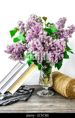 Lilac spring flower bouquet in glass vase on table with rope and books Stock Photo