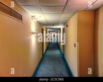 A view of the long hotel corridor, illuminated by a number of lights. Entrances to rooms are visible in the image. Stock Photo