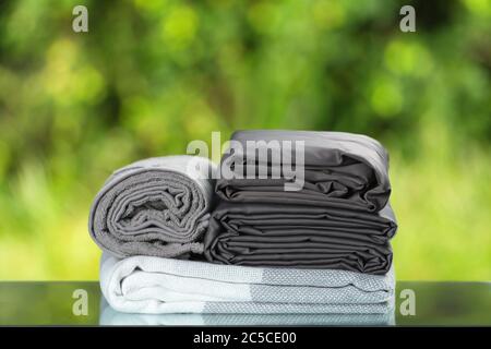 Stack of folded bedding. Monochrome gray gradient plaid towel bedsheet textile set on blurred foliage background. Stock Photo