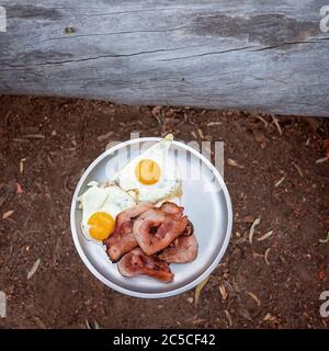 Bacon and eggs served on a tin plate at a campfire bush breakfast on an Australian outback tourist resort Stock Photo