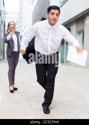 Man is running away from angry businesswoman because she is dissatisfied of the results of the financial report outdoors. Stock Photo