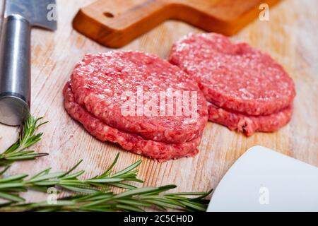 Shaped patties from raw ground meat and fresh greens on wooden background Stock Photo