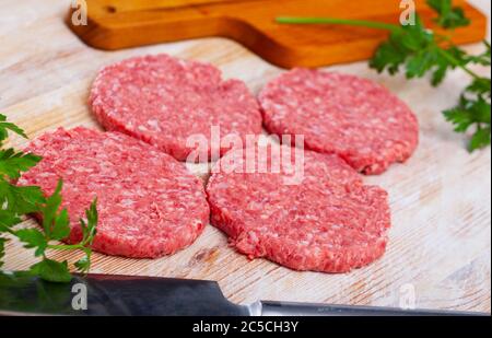 Shaped patties from raw ground meat and fresh greens on wooden background Stock Photo