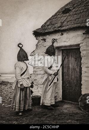 Early 1920's and a re-enactment of Straw Boys knocking on the door of a traditional west coast thatched cottage.With their elaborate woven straw disguises, once a regular sight in many rural parts of the country. Prior to the beginning of the 19th Century, they indulged in illegal activities, but later became frequent visitors to weddings and gradually became a symbol of good luck. Originally photographed by  A. W. Cutler (1875-1935) for 'Ireland: The Rock Whence I Was Hewn', a National Geographic Magazine feature from March 1927. Stock Photo