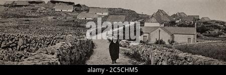 An early 1920's view of a woman in traditional dress walking down a boreen between dry stone walls on Inishmaan, one of the Aran Islands off County Galway on the west coast of Ireland. Originally photographed by  A. W. Cutler (1875-1935) for 'Ireland: The Rock Whence I Was Hewn', a National Geographic Magazine feature from March 1927. Stock Photo