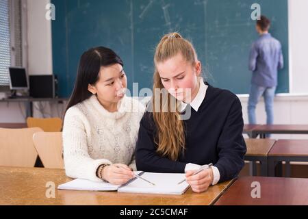 Tired female students during writing notes in classroom,  male student writing on whiteboard Stock Photo