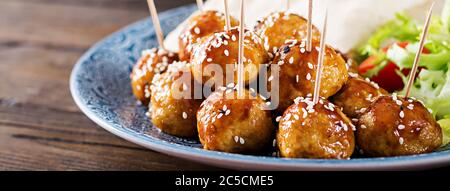 Meatballs in sweet and sour glaze on a plate with pita bread and vegetables in a Moroccan style on a wooden table. Tapas.  Banner. Trend food. Stock Photo
