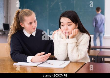 Tired female students during writing notes in classroom,  male student writing on whiteboard Stock Photo