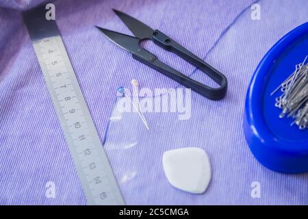 Top view: professional equipment and tools for sewing: pins, thread snips, needles, piece of cloth, chalk, ruler on table at atelier. Fashion Stock Photo