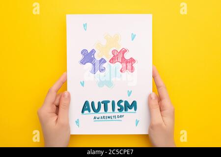 cropped view of woman holding card with puzzle for Autism Awareness Day on yellow Stock Photo