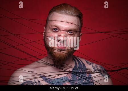 Photo of tangled in black threads bearded angry man Stock Photo