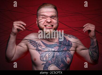 Photo of tangled in black threads bearded blond man Stock Photo