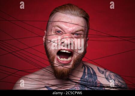 Photo of tangled in black threads bearded screaming man Stock Photo