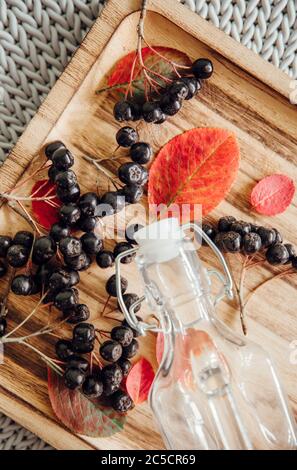 Making Aronia berries (Aronia prunifolia ) also known as chokeberries syrup in autumn. Juice bottle with berries on wooden tray. Stock Photo