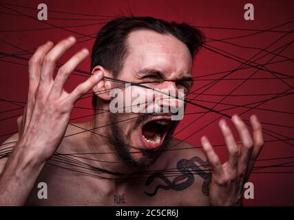 Photo of screaming tangled in black threads brunette man Stock Photo
