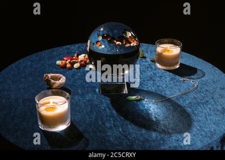 Crystal ball near candles and fortune telling stones on dark blue velour cloth isolated on black Stock Photo