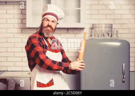 Crazy young male chef cook or baker man in white apron chefs hat posing in kitchen background Stock Photo