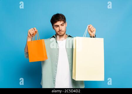 thoughtful young man holding shopping bags on blue Stock Photo