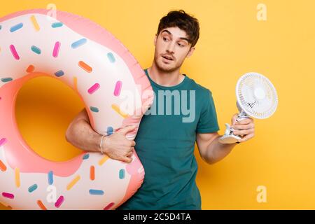 surprised man holding inflatable donut and little electric fan on yellow Stock Photo