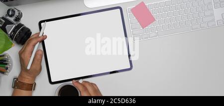 Overhead shot of male left hand using mock-up tablet while right hand holding coffee cup on white office desk Stock Photo