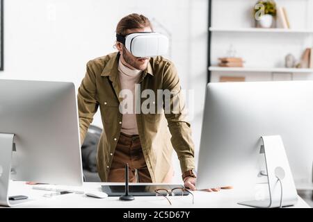 Digital designer in virtual reality headset standing near computers and graphics tablet on table Stock Photo