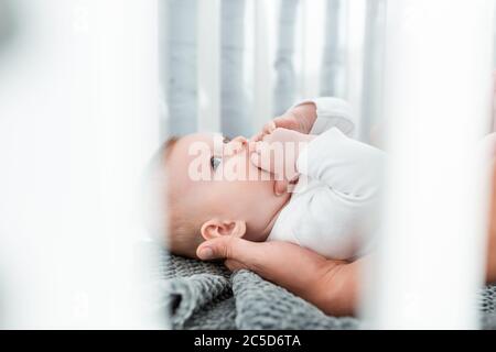 cropped view of man touching cute infant lying in baby cot, selective focus Stock Photo