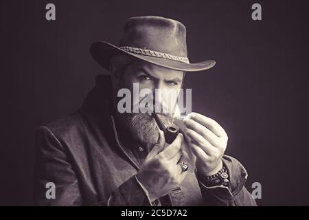 Elegant brutal young man smokes a pipe on the dark place Stock Photo