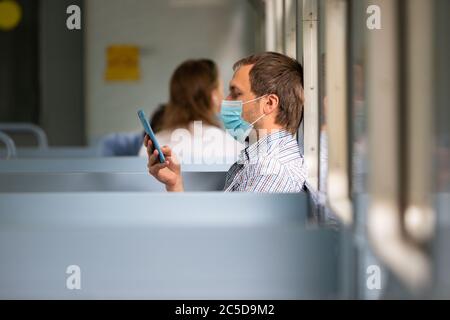 Man using smartphone, wears a protective mask in train to protect the respiratory system from coronavirus infection, covid-19. Preventive measure. New Stock Photo