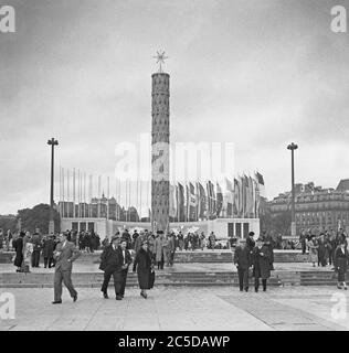 A view of the 1937 Expo (World's Fair or Exposition) held in Paris, France – here people are entering the site at its north end, The Trocadero. The tall tower has the word 'Pax' (Peace) at its base and the flags of nations flutter in the breeze – including the German flag with its swastika. Stock Photo