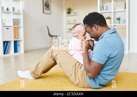 Young African father sitting on the floor and playing with his baby daughter in the room at home Stock Photo