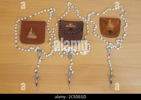 Three plain white sets of rosary beads with Lourdes and personal wallet Stock Photo