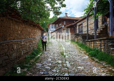 Old Bulgarian lady with hands behind back walking up cobbled sttreet in Zheravna village Bulgaria Stock Photo