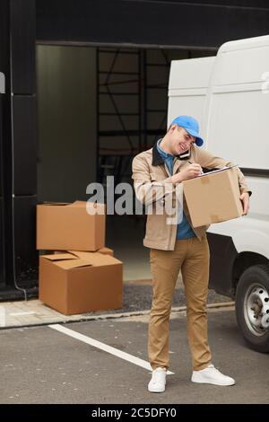 Young man talking on mobile phone while working with load in warehouse Stock Photo