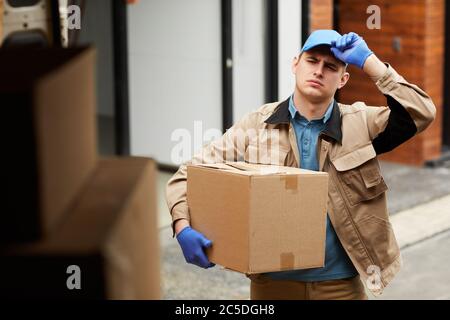 Young man in uniform carrying cardboard box to the van he loading the parcels Stock Photo