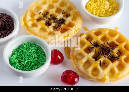 Mini waffles, cake sprinkles and cherries on white background - syrupy waffles Stock Photo