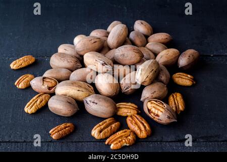 Pecan nuts in shell, cracked and halves isolated on rustic black wooden plank background Stock Photo