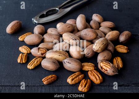 Pecan nuts in shell, cracked and halves isolated on rustic black wooden background with de-focused nutcracker in background Stock Photo