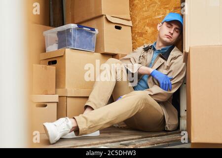 Young courier in uniform resting in the car he tired after work Stock Photo